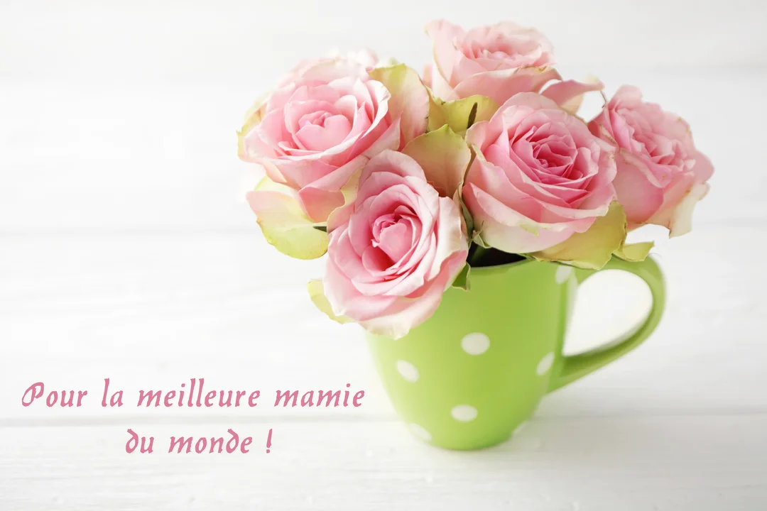 Un bouquet de roses roses délicates est présenté dans un mug vert à pois blancs, posé sur une surface en bois peinte en blanc.