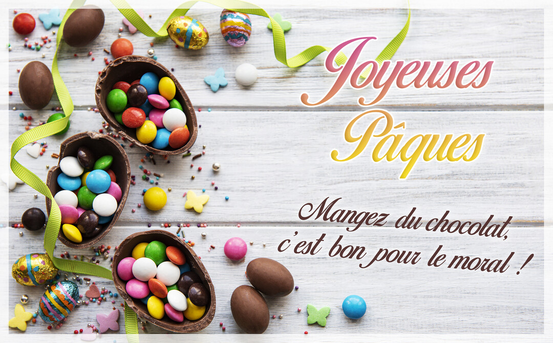 Vue de dessus d'œufs en chocolat et de bonbons de Pâques multicolores, disposés sur une surface en bois blanc avec un ruban vert.