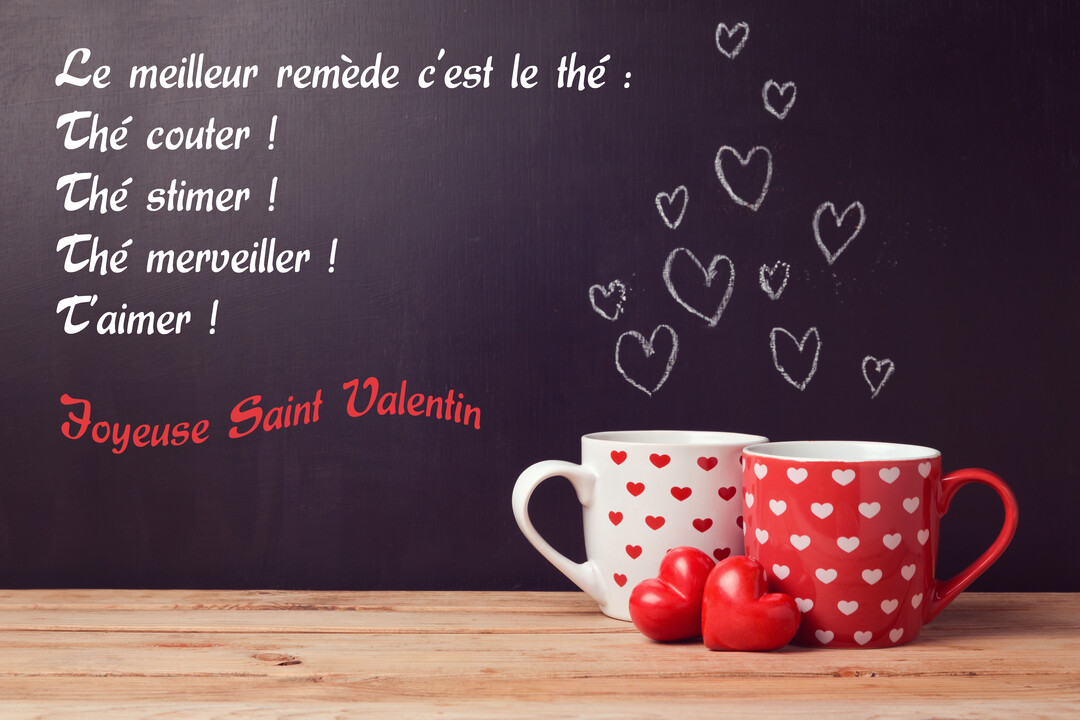 Sur une table en bois, deux mugs à motifs de cœurs sont posés devant un tableau noir où est écrit un poème d'amour humoristique.