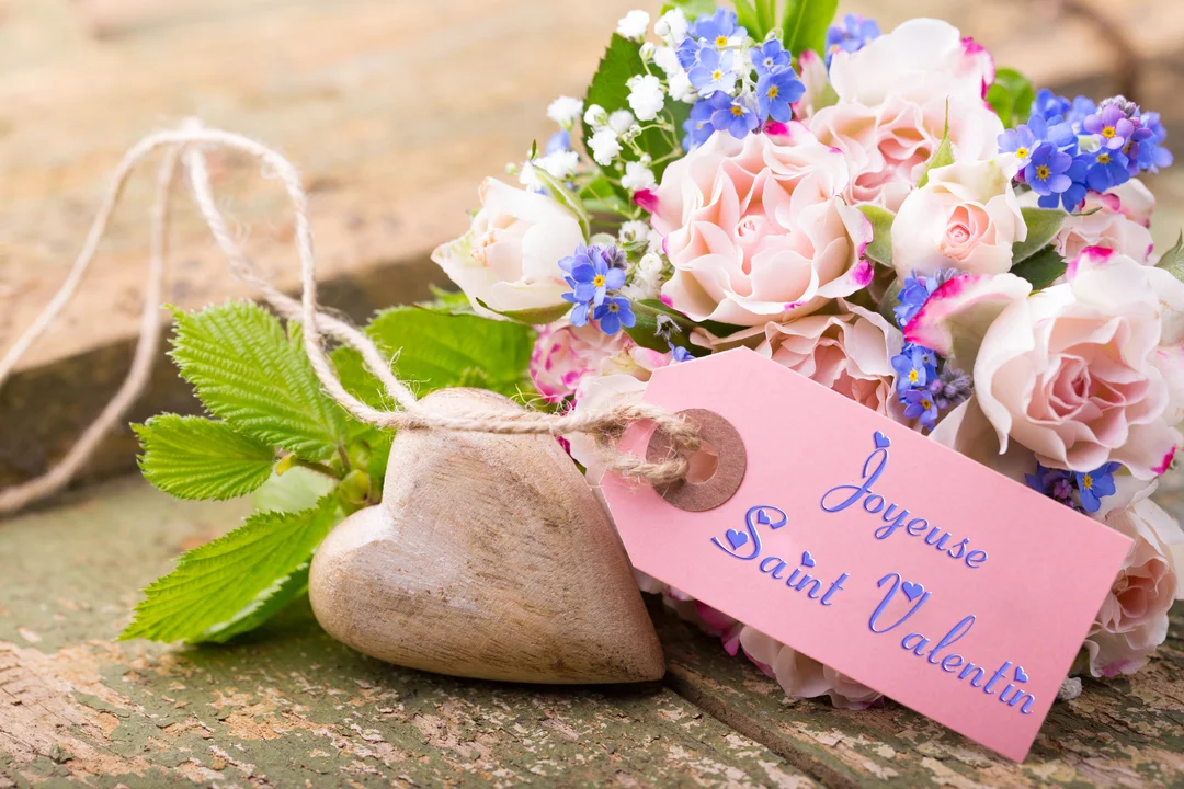 Un bouquet de roses et de fleurs bleues est posé sur une table en bois rustique à côté d'un cœur en bois sculpté.
