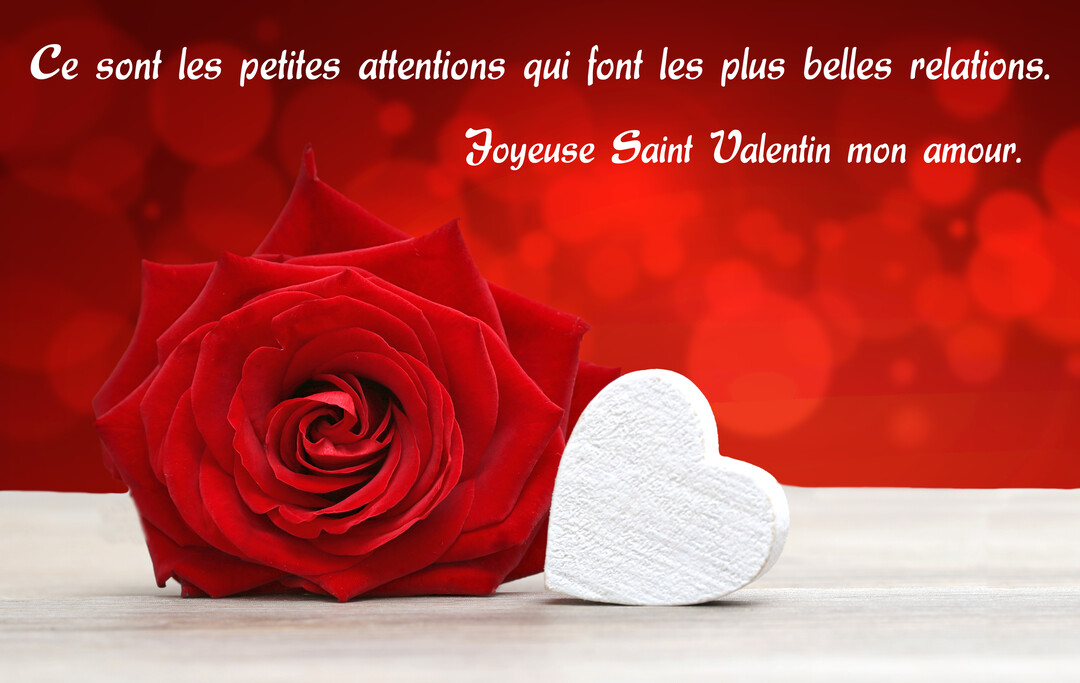 Une rose rouge et un cœur blanc sont posés sur une surface en bois, avec un fond rouge lumineux et flouté.