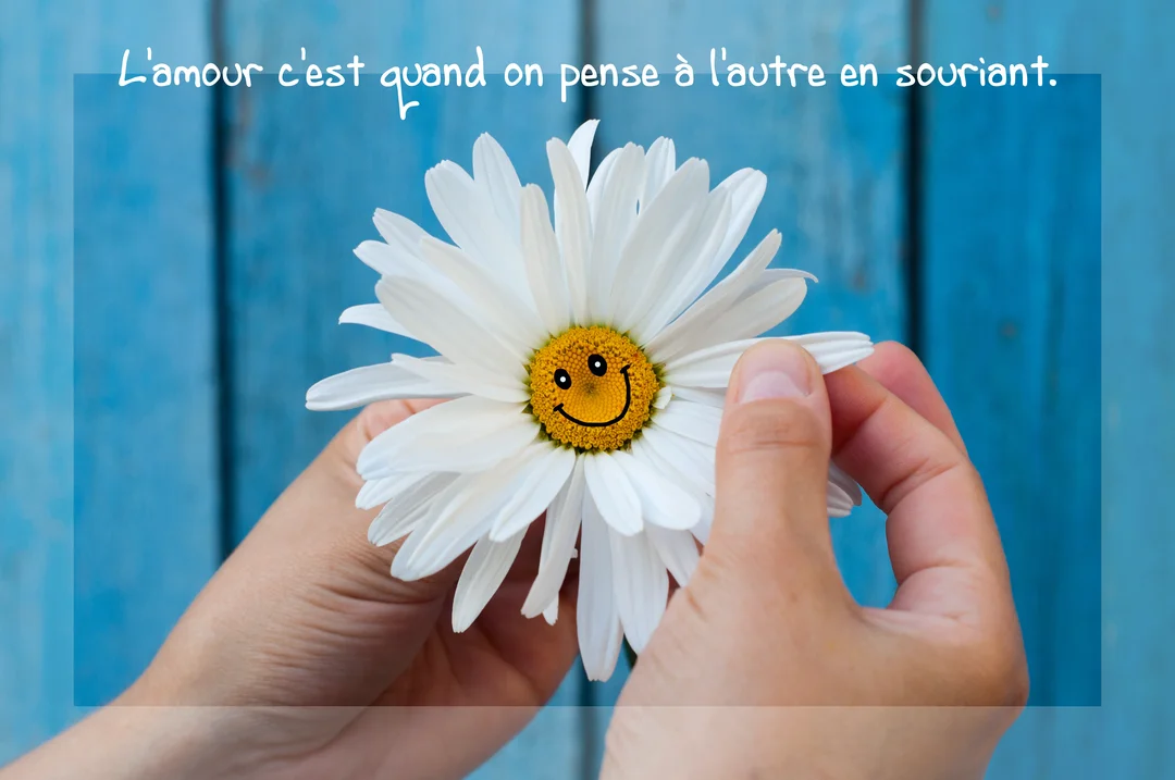 Deux mains tiennent délicatement une marguerite dont le cœur jaune est dessiné d'un visage souriant, sur un fond de planches en bois bleu.