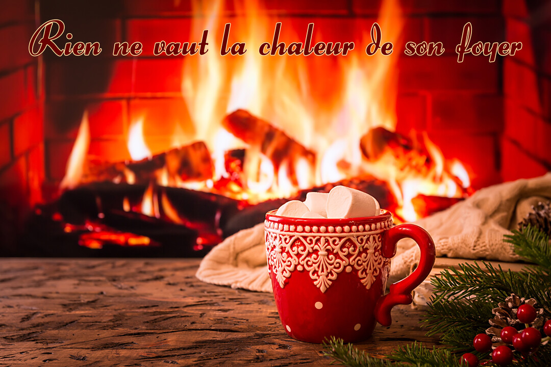 Au premier plan, une tasse rouge avec des guimauves est posée devant un feu de cheminée chaleureux en arrière-plan flouté.