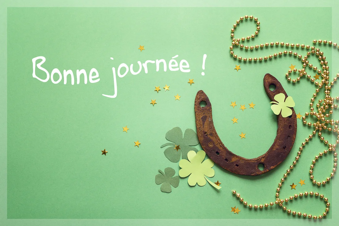 Composition à plat sur fond vert avec un fer à cheval, des trèfles en papier, des perles dorées et le texte manuscrit 'Bonne journée'.