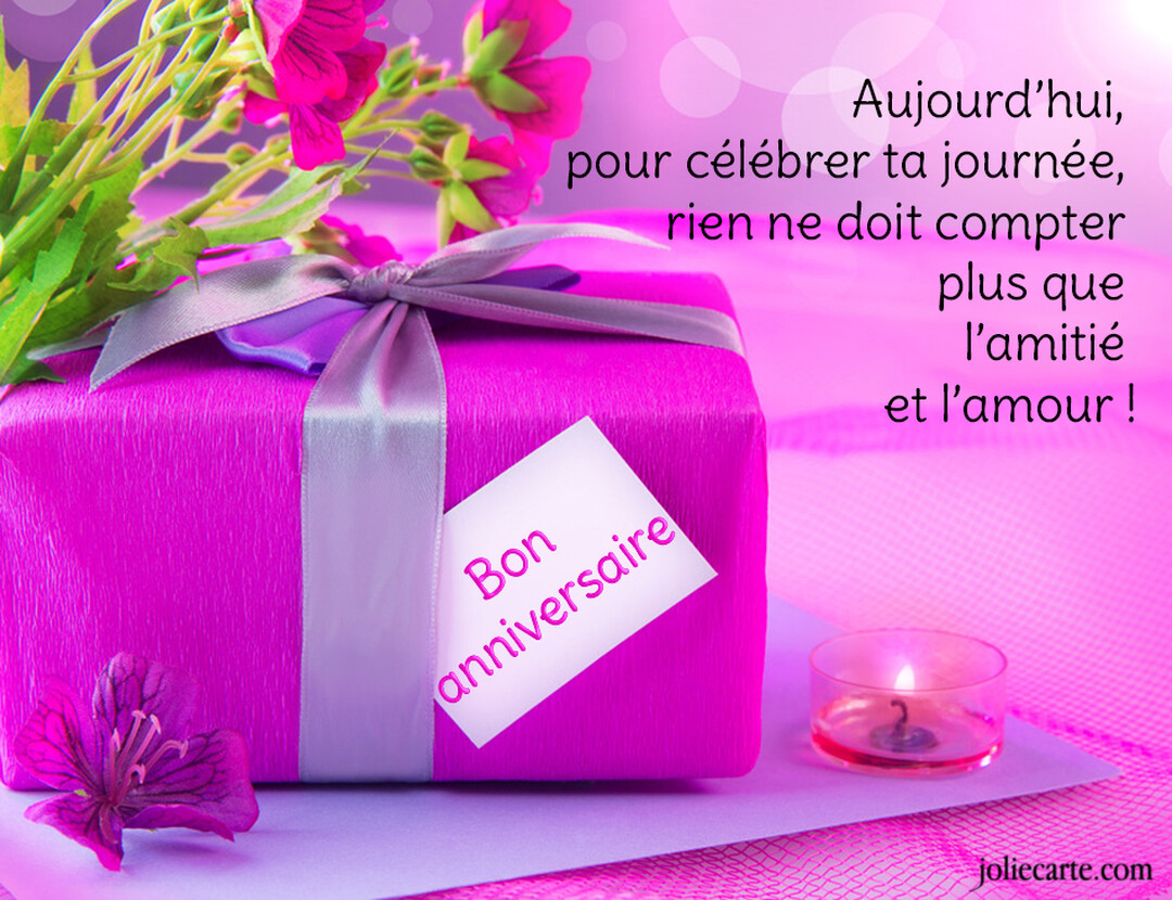 Une scène festive d'anniversaire avec un cadeau emballé en rose, des fleurs, une bougie allumée et une étiquette 'Bon anniversaire' sur fond rose.