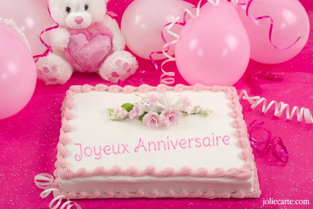 Une scène de fête d'anniversaire rose avec un gâteau rectangulaire, un ours en peluche blanc et des ballons sur une nappe pailletée.