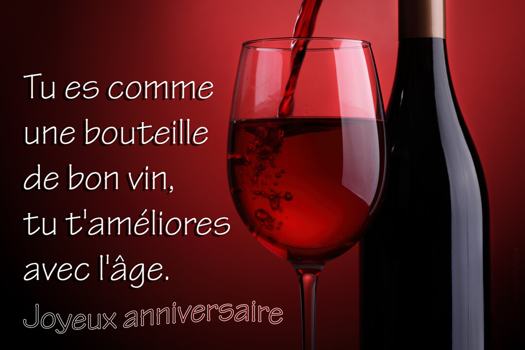 Sur un fond rouge dégradé, du vin rouge est versé dans un verre ballon à côté d'une bouteille de vin sombre.