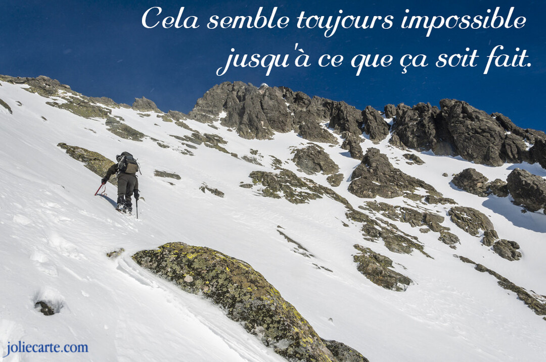 Un alpiniste équipé progresse avec difficulté sur une pente abrupte et enneigée en direction du sommet d'une montagne sous un ciel dégagé.