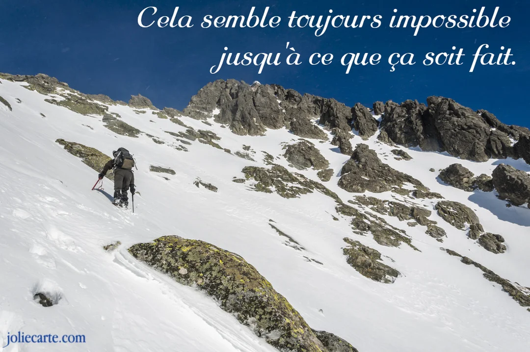 Un alpiniste équipé progresse avec difficulté sur une pente abrupte et enneigée en direction du sommet d'une montagne sous un ciel dégagé.