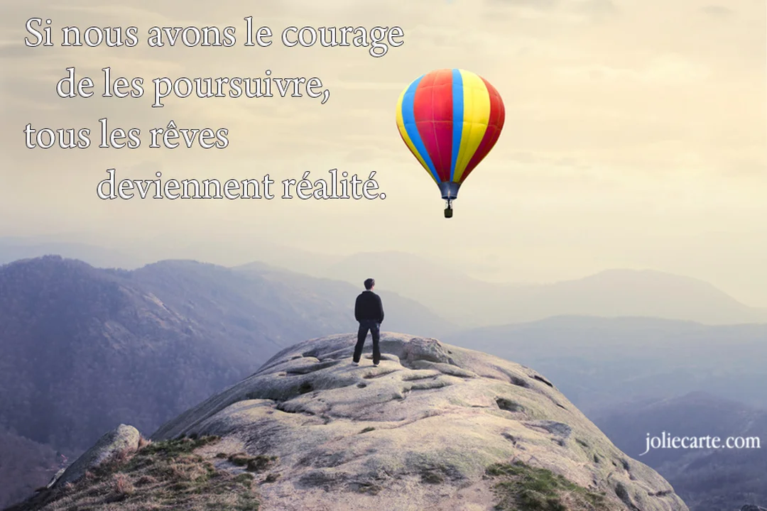 Un homme debout sur un pic rocheux contemple un vaste paysage montagneux, tandis qu'une montgolfière vivement colorée flotte dans un ciel brumeux.