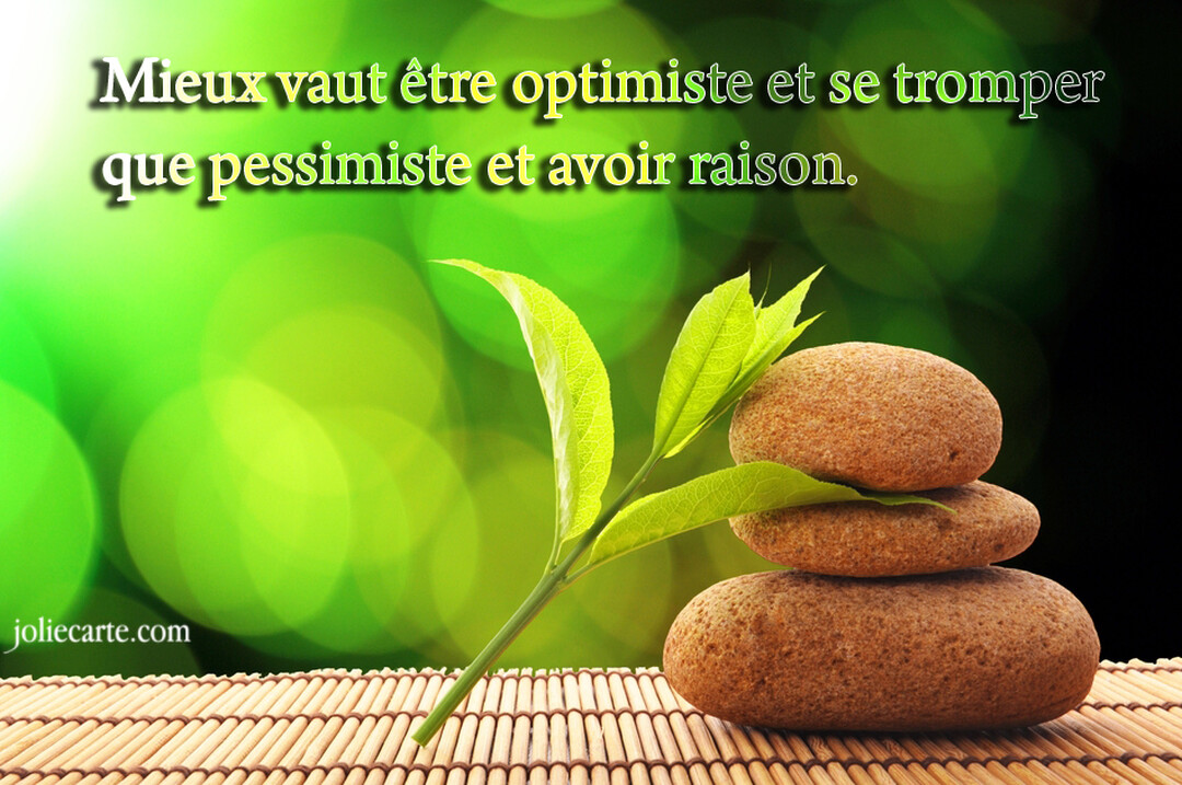 Trois galets bruns sont empilés en équilibre à côté d'une jeune pousse verte, sur une natte de bambou avec un fond vert flouté.
