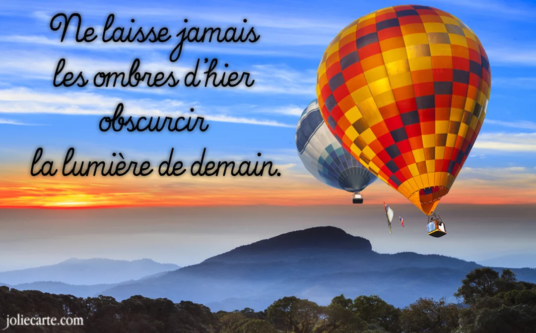 Deux montgolfières, l'une très colorée, flottent dans un ciel de lever de soleil au-dessus d'un paysage montagneux et brumeux.