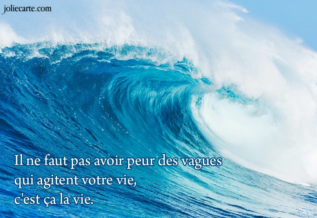 Une photographie impressionnante d'une énorme vague océanique qui se creuse et déferle, avec son sommet couronné d'écume blanche sous un ciel bleu.