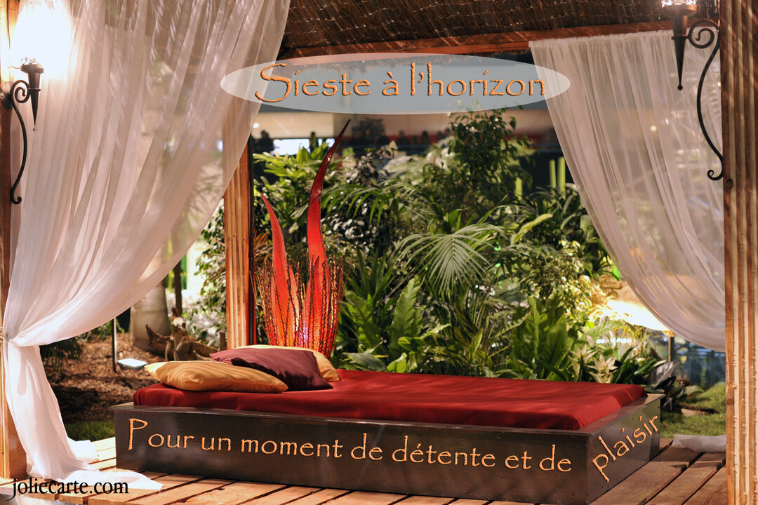 Une scène d'intérieur exotique montre un lit de repos avec un matelas rouge sous des voilages blancs, près d'une végétation luxuriante.