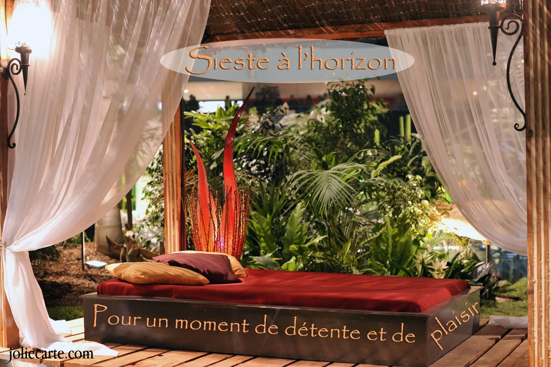 Une scène d'intérieur exotique montre un lit de repos avec un matelas rouge sous des voilages blancs, près d'une végétation luxuriante.