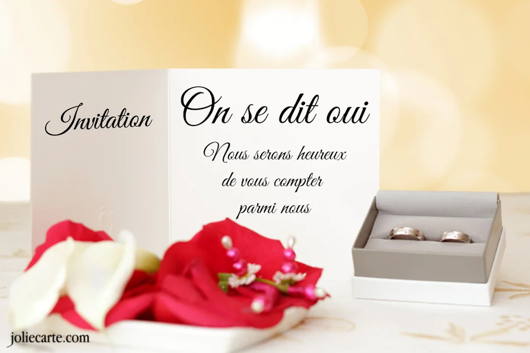 Une carte de faire-part de mariage est posée à côté d'un écrin contenant des alliances, sur un fond lumineux avec des pétales rouges.