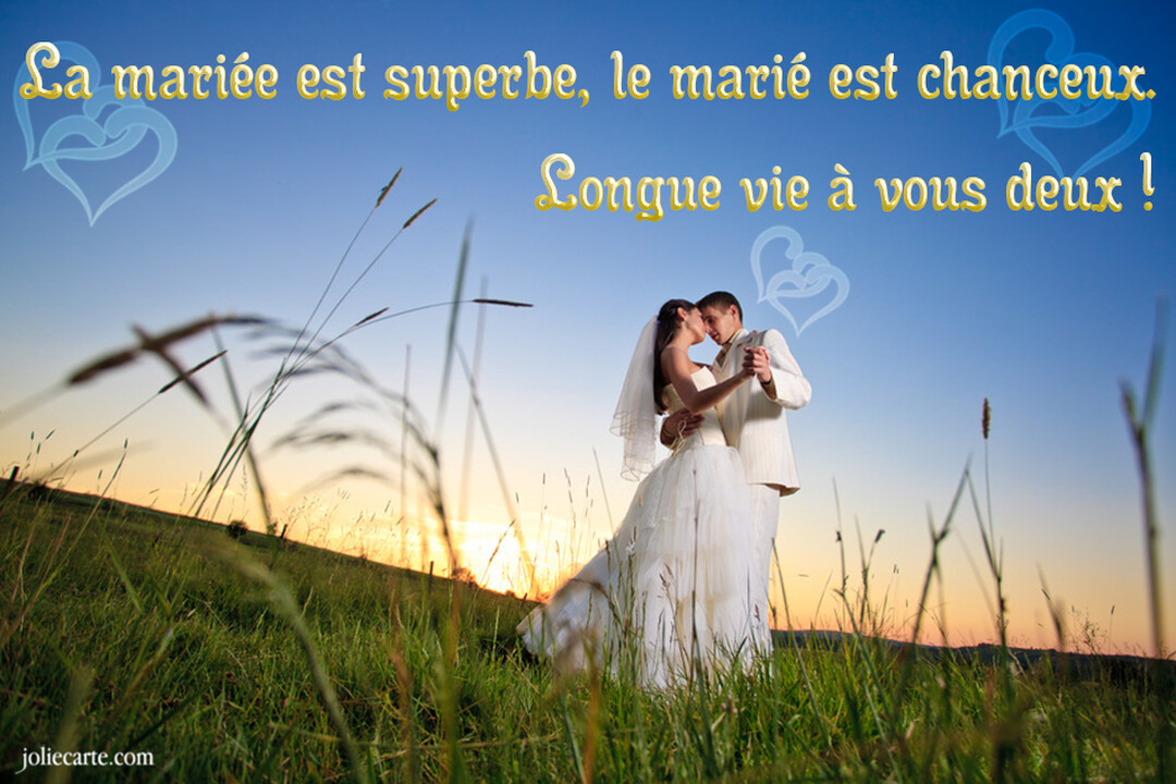 Un couple de jeunes mariés, la mariée en robe blanche et le marié en costume clair, danse tendrement dans une prairie au crépuscule.