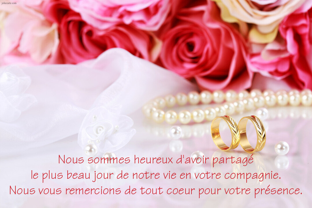 Deux alliances dorées gravées sont posées au premier plan, accompagnées de perles nacrées, avec un bouquet de roses roses en arrière-plan flou.