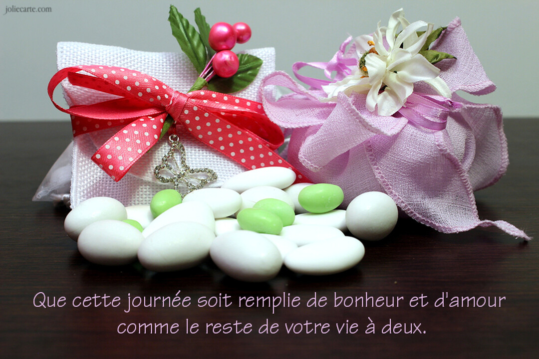 Une composition de dragées de mariage blanches et vertes avec deux ballotins décorés de rubans et de fleurs, sur une surface en bois.