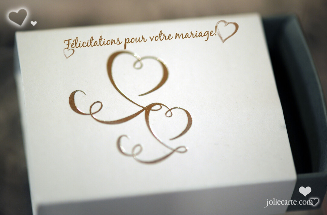 Gros plan sur le couvercle d'une petite boîte blanche où sont inscrits en doré 'Félicitations pour votre mariage' et des cœurs stylisés.