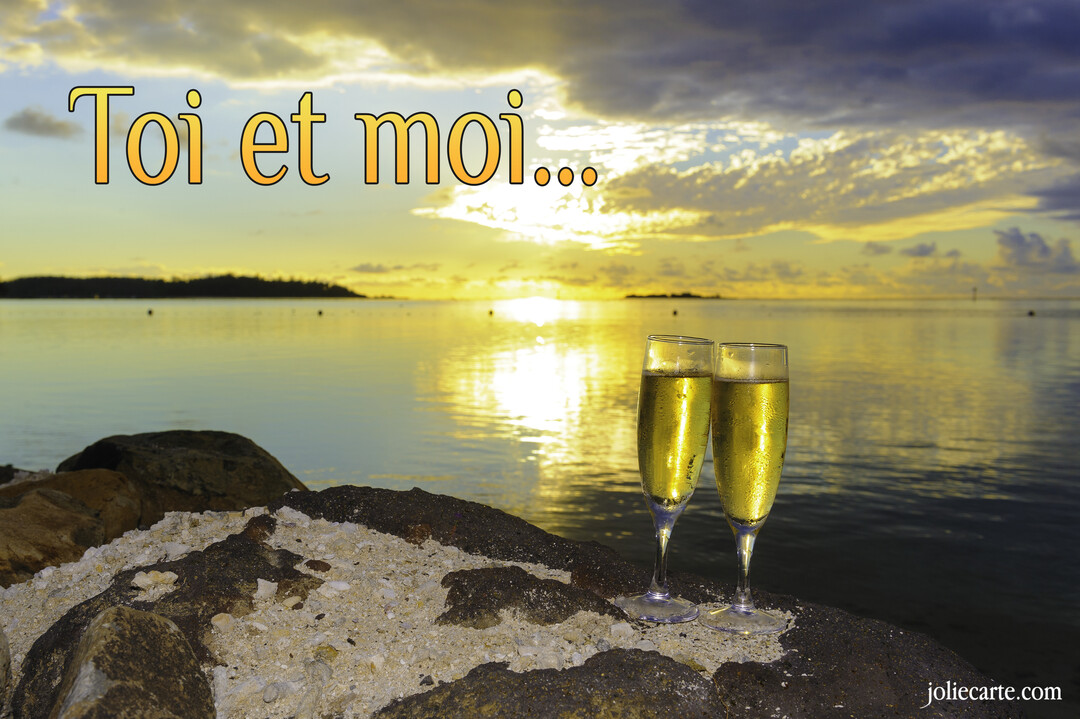 Deux coupes de champagne sont posées sur des rochers au bord de l'eau, avec un magnifique coucher de soleil se reflétant sur la mer.