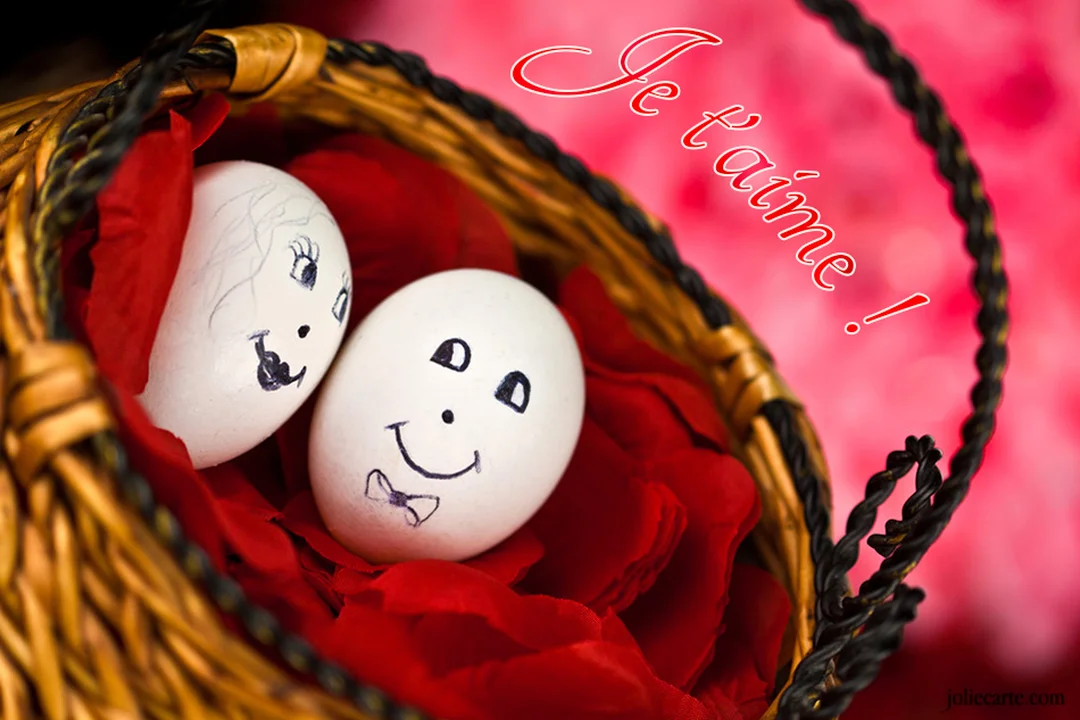 Un couple d'œufs décorés avec des visages souriants repose dans un panier en osier, sur un lit de pétales rouges vifs.