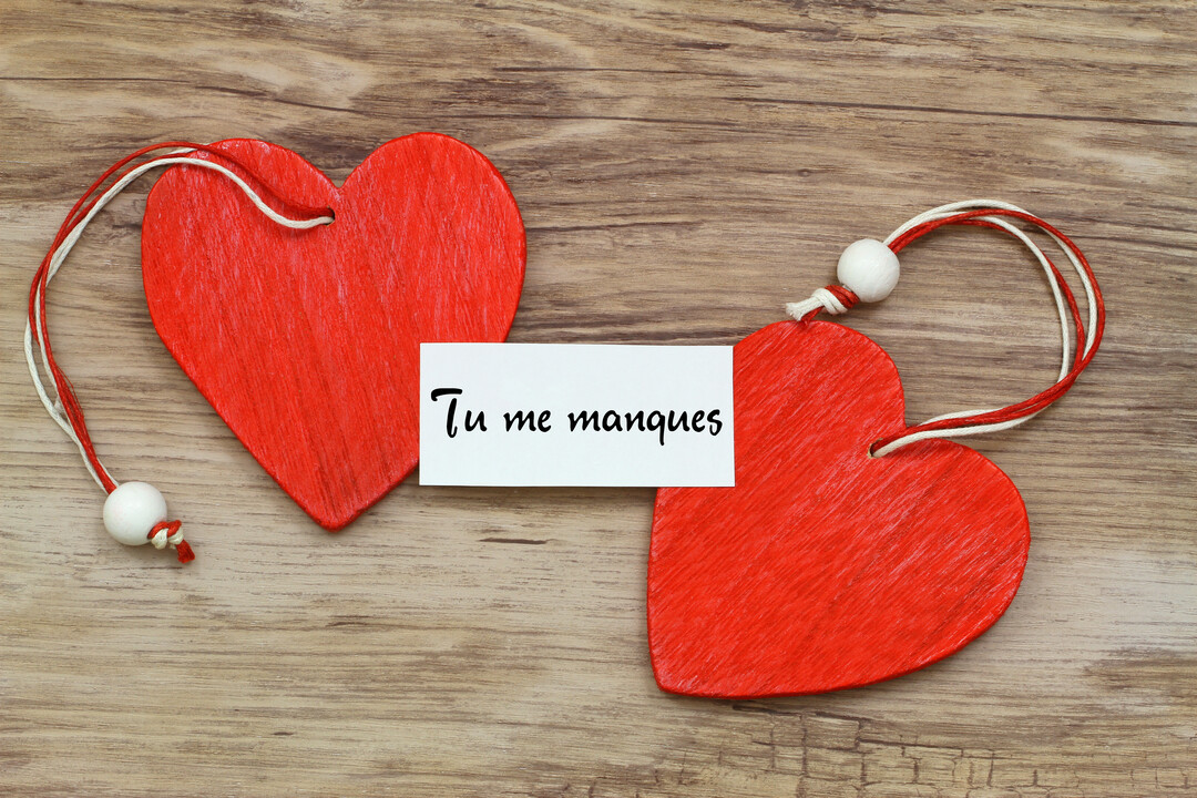 Deux décorations en forme de cœur, peintes en rouge, reposent sur un fond en bois texturé, accompagnées d'un petit mot 'Tu me manques'.