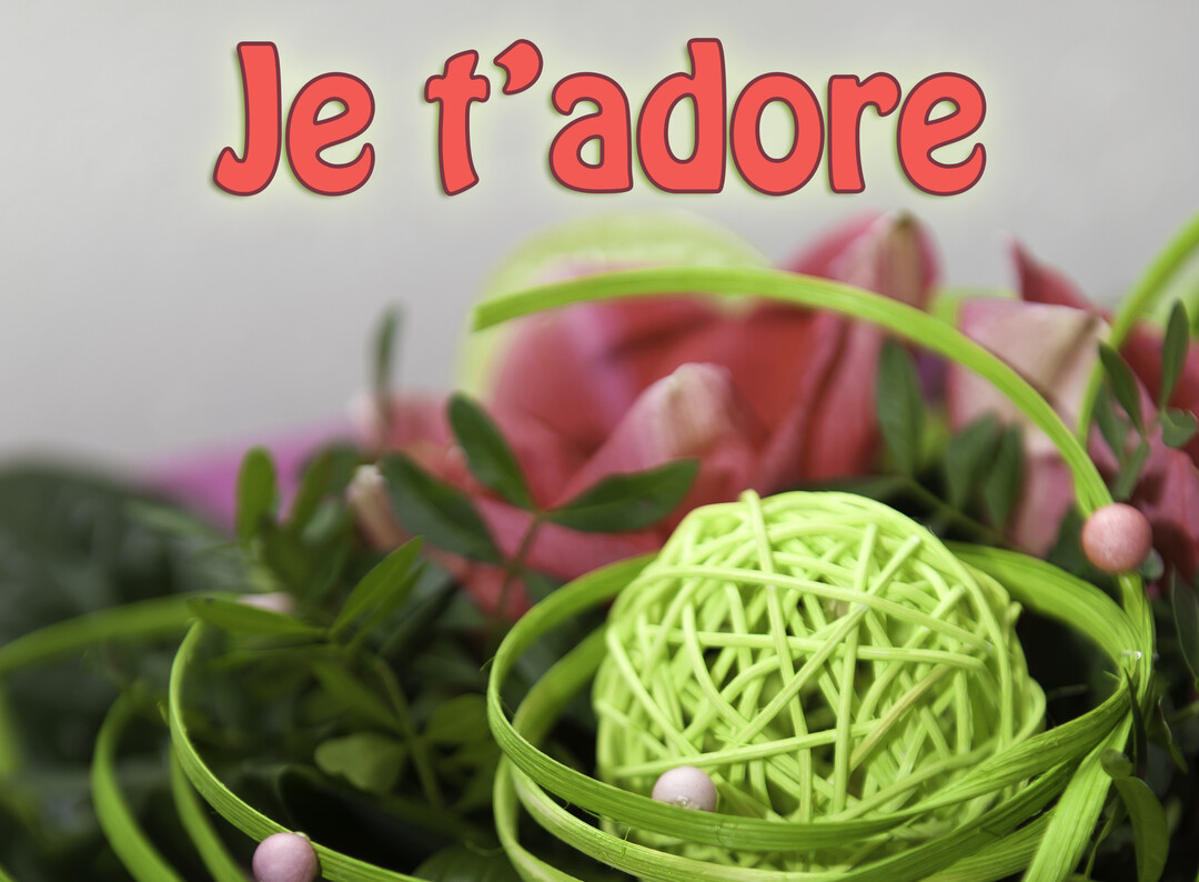 Un gros plan sur une composition florale moderne avec des tulipes roses, du feuillage vert et une boule décorative en osier vert.