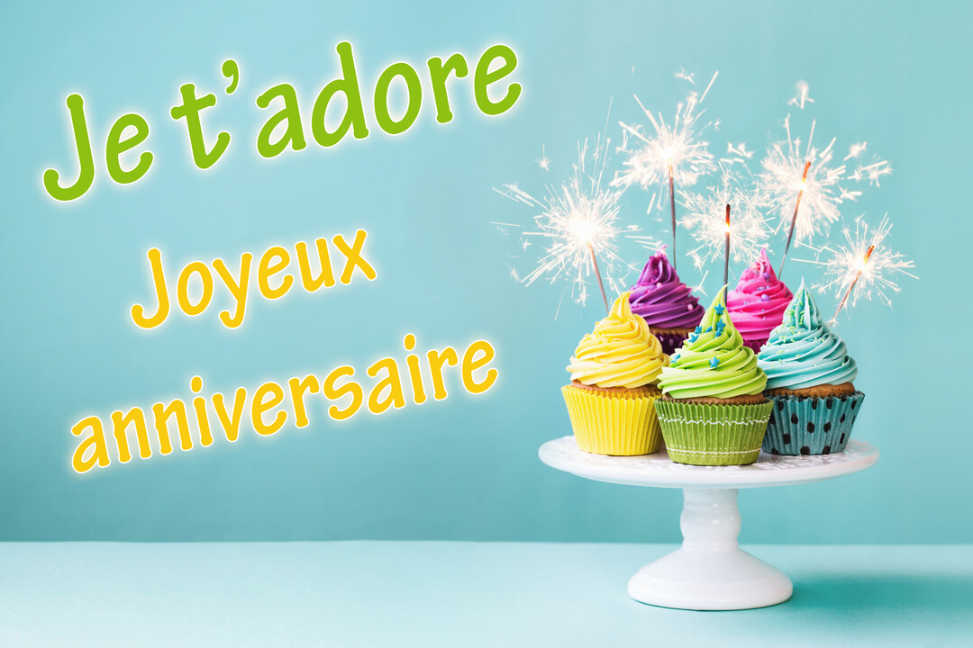 Sur un fond bleu-vert, un présentoir blanc soutient six cupcakes colorés surmontés de glaçage et de cierges magiques allumés.