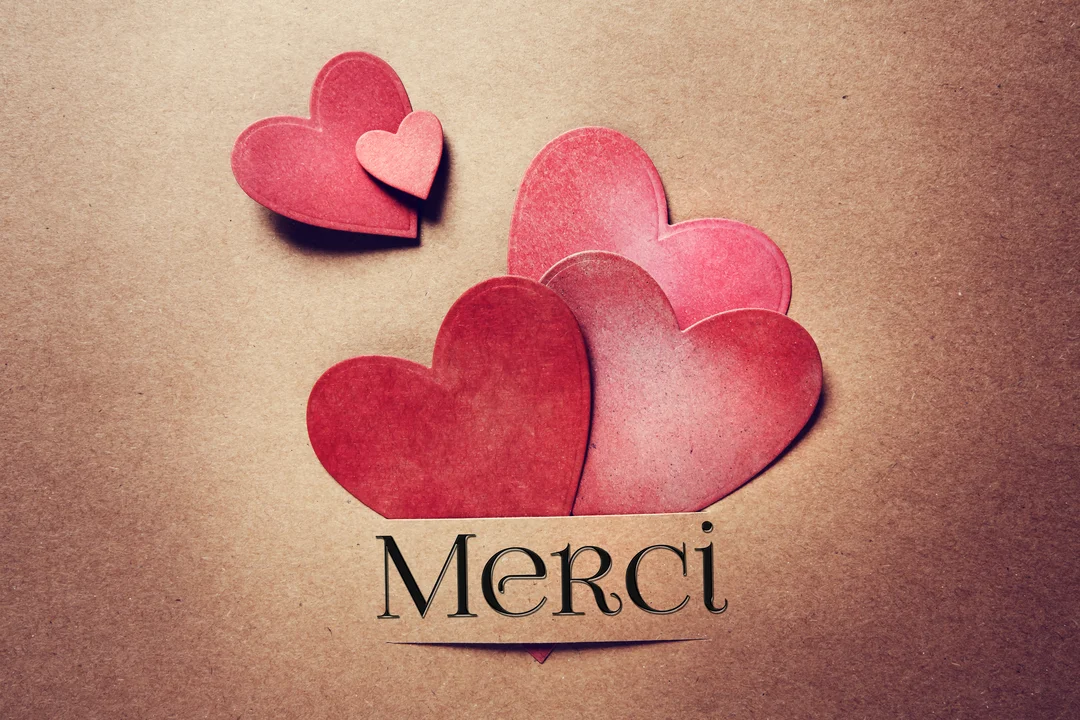 Une composition de plusieurs cœurs en papier rouge et rose sur un fond texturé brun, avec une banderole affichant le mot 'Merci'.