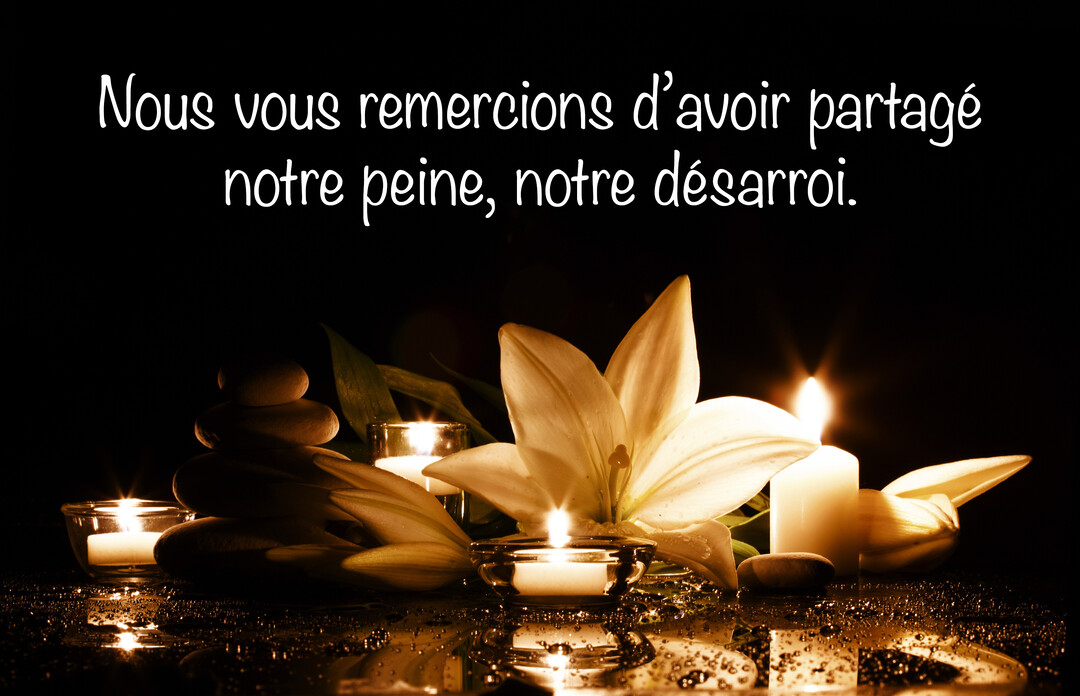 Sur un fond noir, des bougies allumées et une fleur de lys blanc sont posées sur une surface réfléchissante mouillée, à côté de galets empilés.