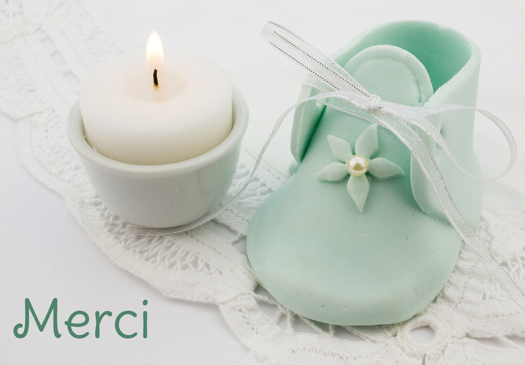 Une composition délicate montre un chausson de bébé vert d'eau et une bougie allumée sur de la dentelle blanche, symbolisant une cérémonie de baptême.