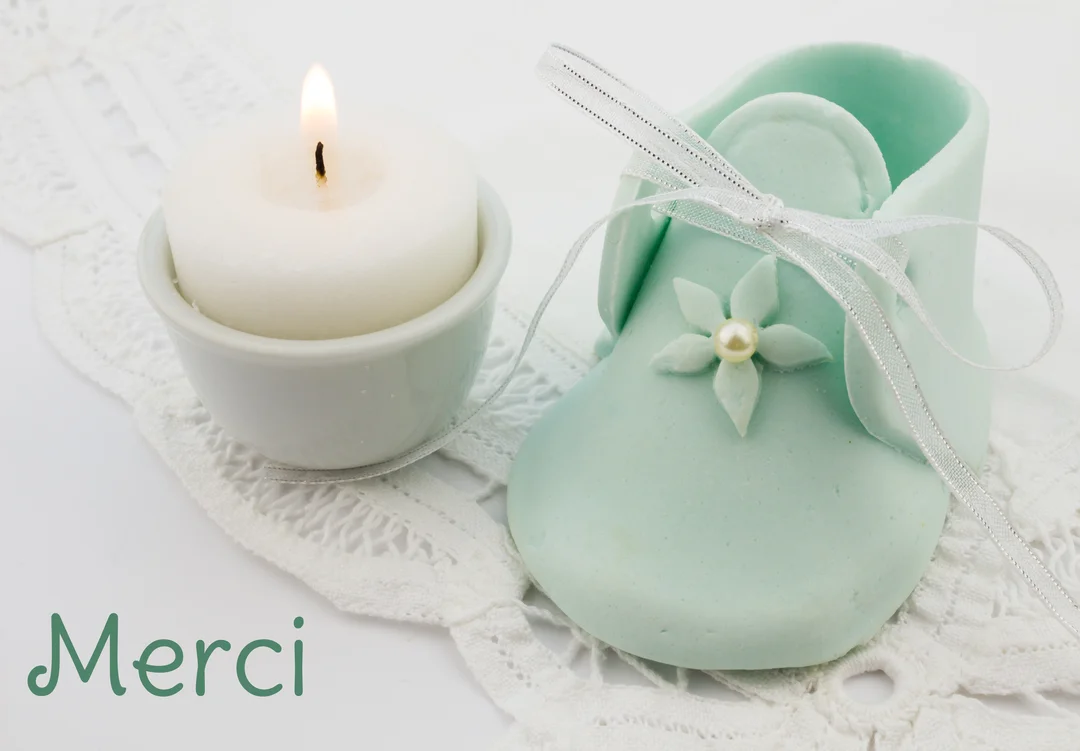 Une composition délicate montre un chausson de bébé vert d'eau et une bougie allumée sur de la dentelle blanche, symbolisant une cérémonie de baptême.