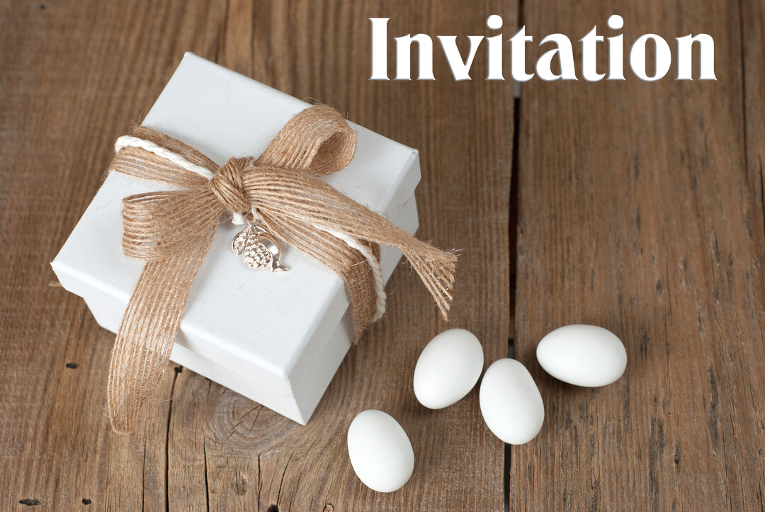 Une boîte cadeau blanche décorée d'un ruban rustique est posée sur une table en bois à côté de quelques dragées blanches.