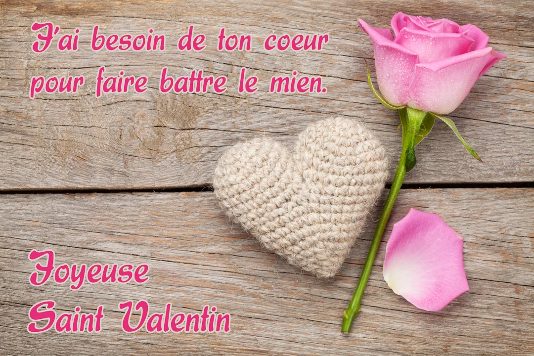 Sur une table en bois, une rose rose est posée à côté d'un cœur en tricot beige et d'un texte d'amour romantique.