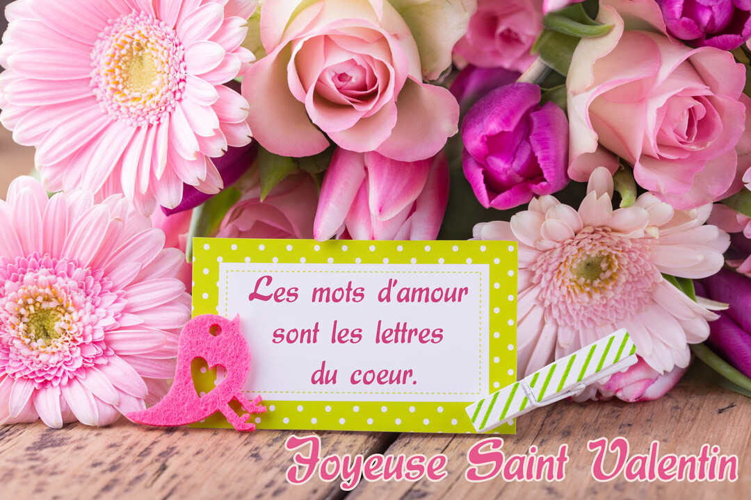 Un bouquet de fleurs roses et un message d'amour pour la Saint-Valentin sont posés sur une table en bois rustique.