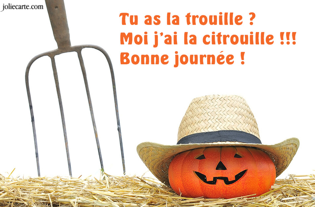 Sur un lit de paille, une citrouille d'Halloween sculptée avec un sourire et coiffée d'un chapeau, accompagnée d'une fourche sur fond blanc.