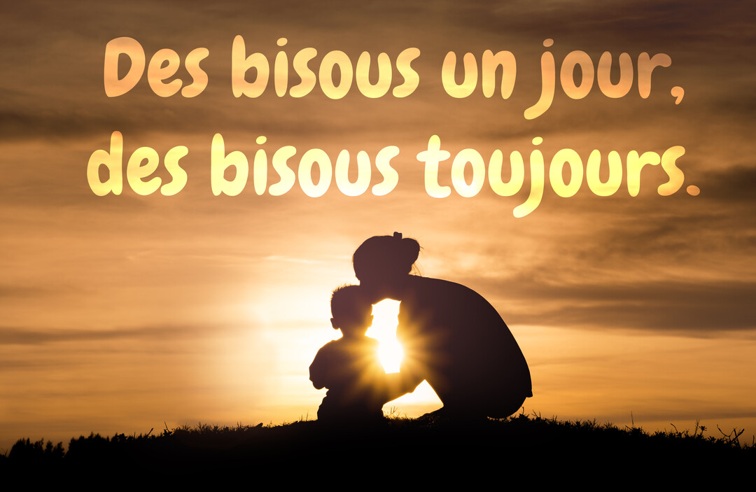 En contre-jour, la silhouette d'une mère embrasse son jeune enfant sur une colline, devant un soleil rayonnant à l'horizon.