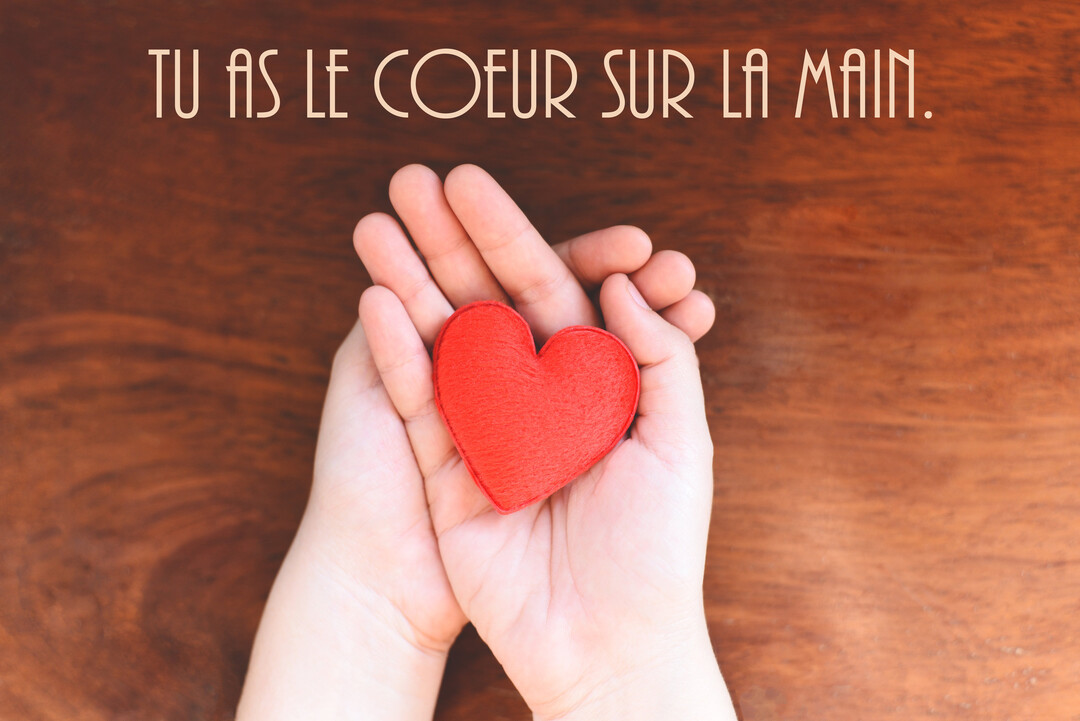 Vue de dessus de deux mains ouvertes tenant un petit cœur en feutrine rouge, sur une surface en bois sombre et texturé.