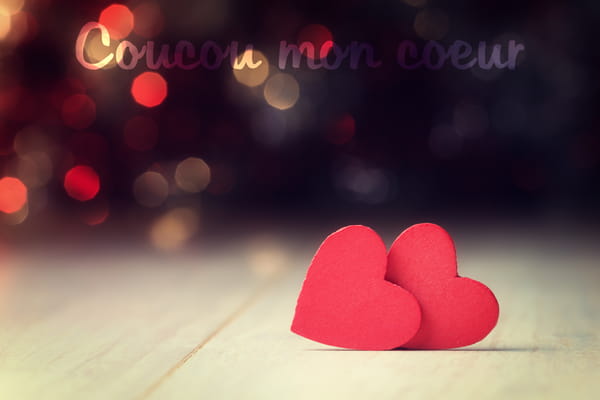 Carte virtuelle avec deux coeurs rouges en papier posés sur une table. En arrière-plan, des lumières floues et chaleureuses. Texte : 'Coucou mon coeur'.