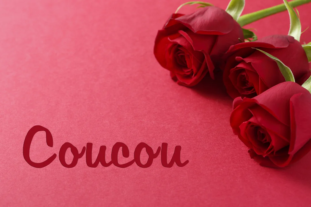 Une photographie en gros plan de trois roses rouges reposant dans le coin supérieur droit sur un fond rouge avec le mot 'Coucou'.