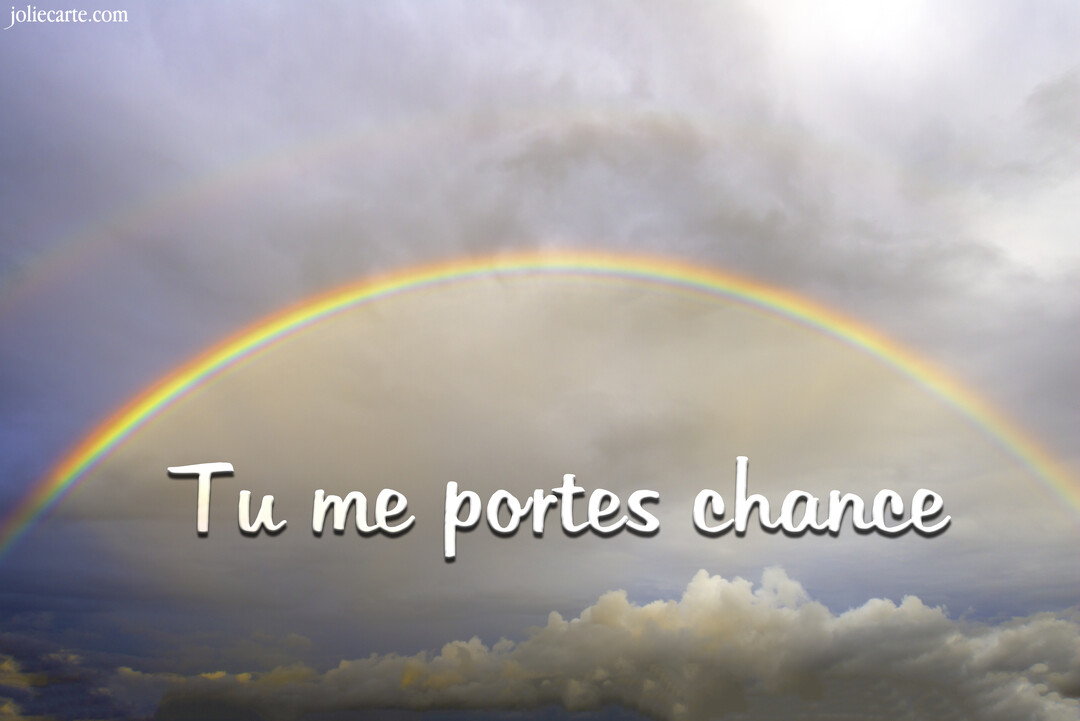 Un double arc-en-ciel aux couleurs vives se déploie dans un ciel rempli de nuages gris et blancs, avec le texte 'Tu me portes chance' au centre.