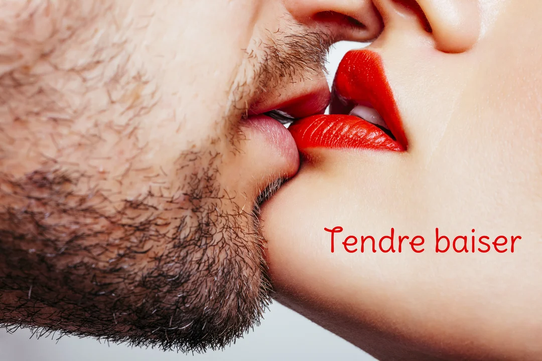 En très gros plan, les lèvres d'un homme barbu et d'une femme au rouge à lèvres carmin se touchent dans un baiser passionné.