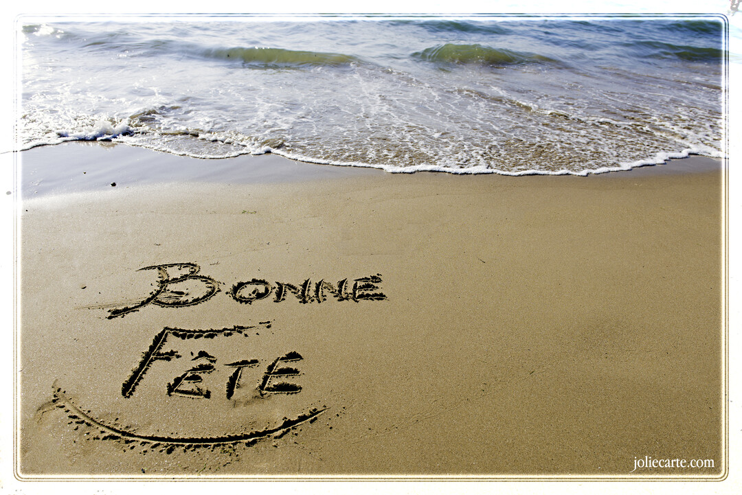 Photographie d'une plage où les mots 'Bonne Fête' sont dessinés sur le sable mouillé, avec une vague approchant doucement du rivage.