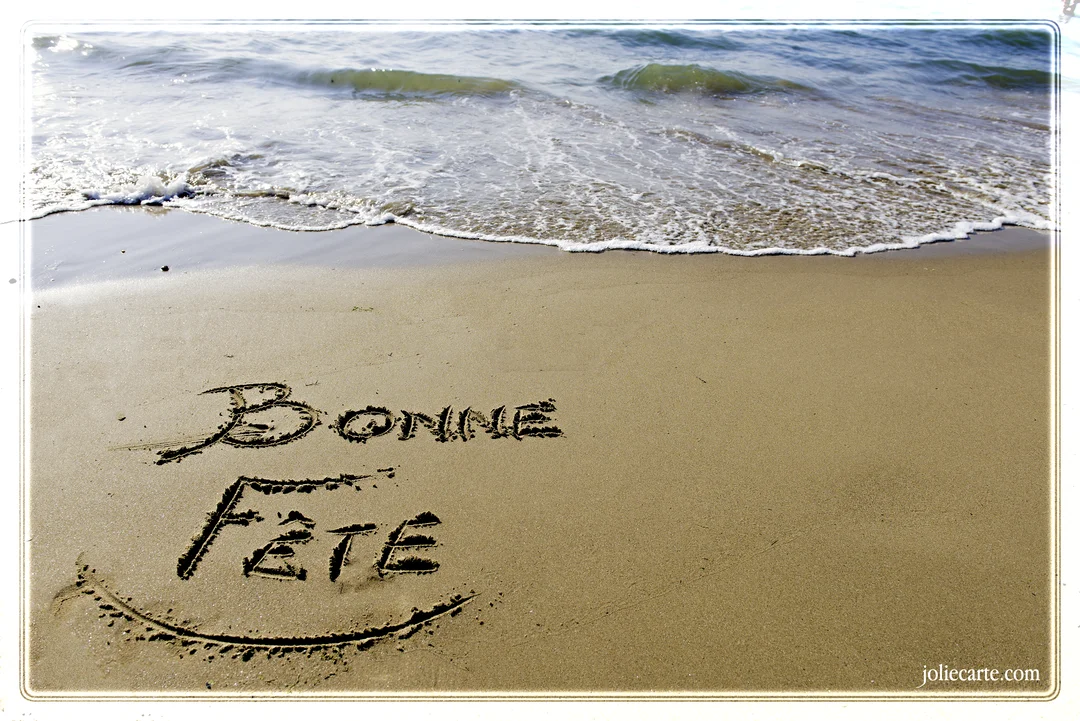 Photographie d'une plage où les mots 'Bonne Fête' sont dessinés sur le sable mouillé, avec une vague approchant doucement du rivage.