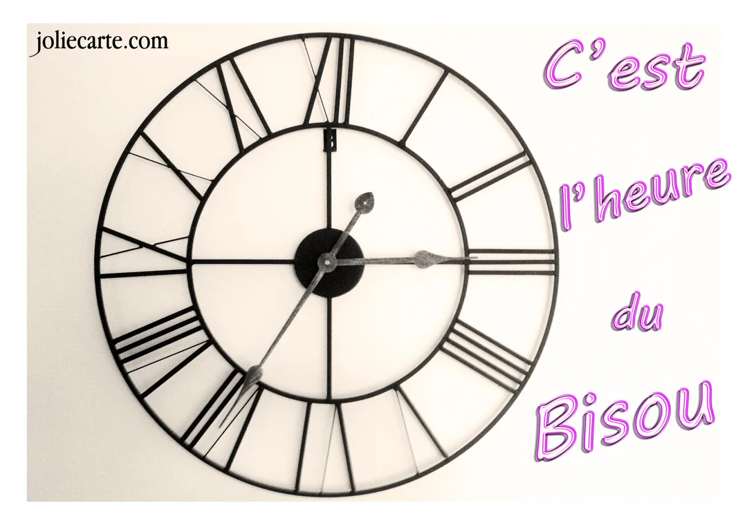 Une horloge murale noire de style vintage sur fond blanc, accompagnée du texte fantaisie rose 'C'est l'heure du bisou'.