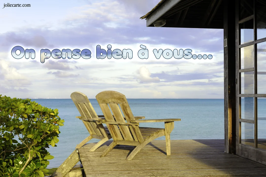 Deux chaises longues en bois sont posées sur une terrasse donnant sur une mer calme et un ciel nuageux au lever du soleil.