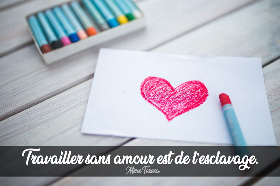 Un cœur rouge dessiné au crayon sur une feuille blanche, posée sur une table en bois clair à côté d'une boîte de crayons de couleur.