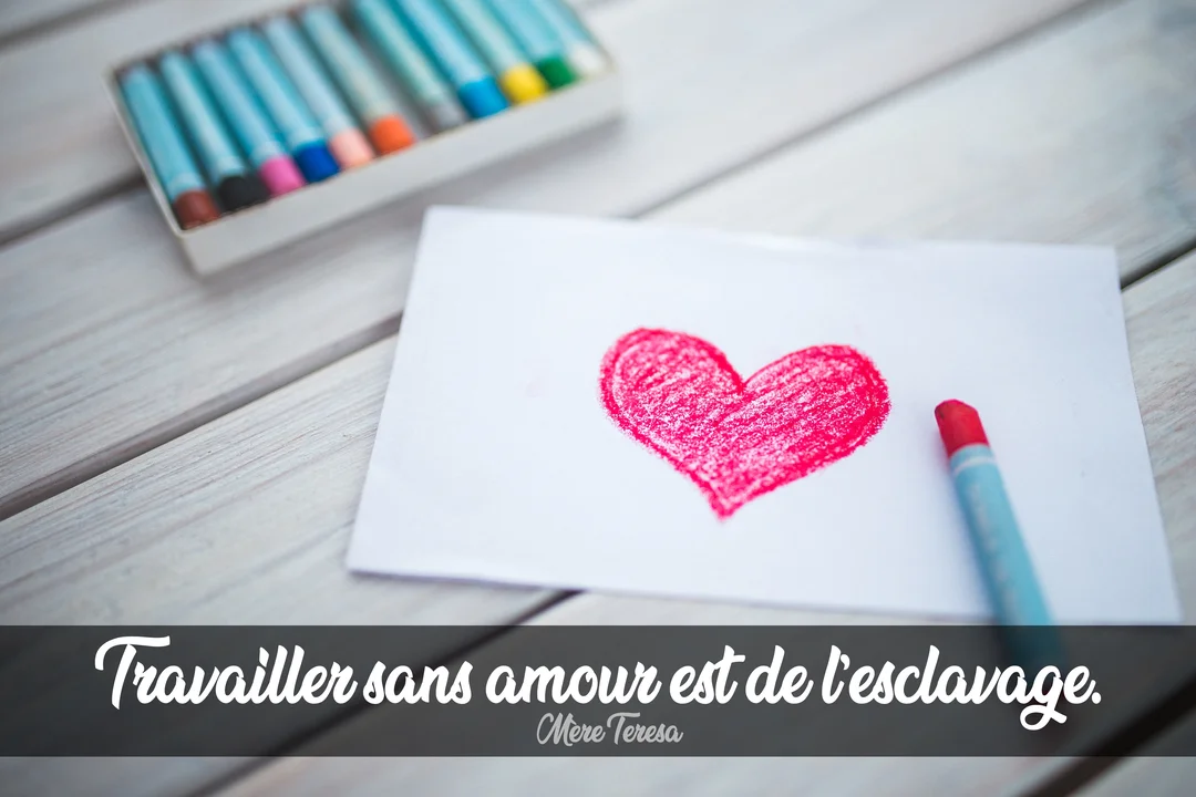 Un cœur rouge dessiné au crayon sur une feuille blanche, posée sur une table en bois clair à côté d'une boîte de crayons de couleur.