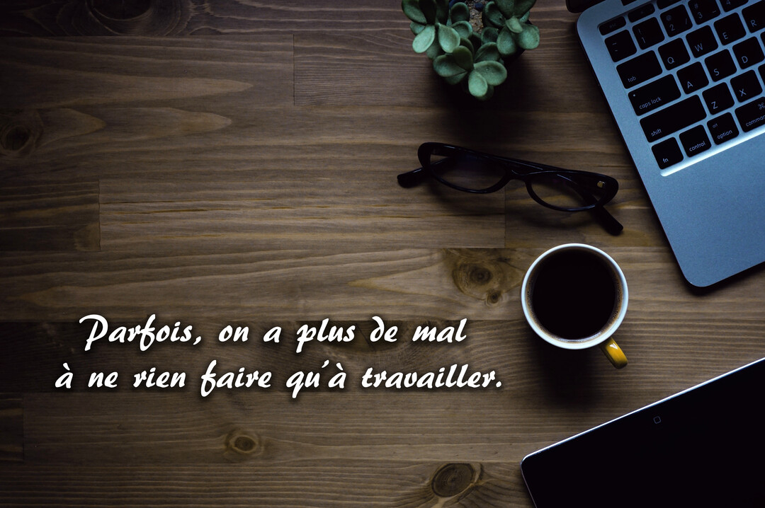 Vue de dessus d'un bureau en bois sur lequel sont posés un ordinateur portable, une tasse de café, des lunettes et une petite plante.